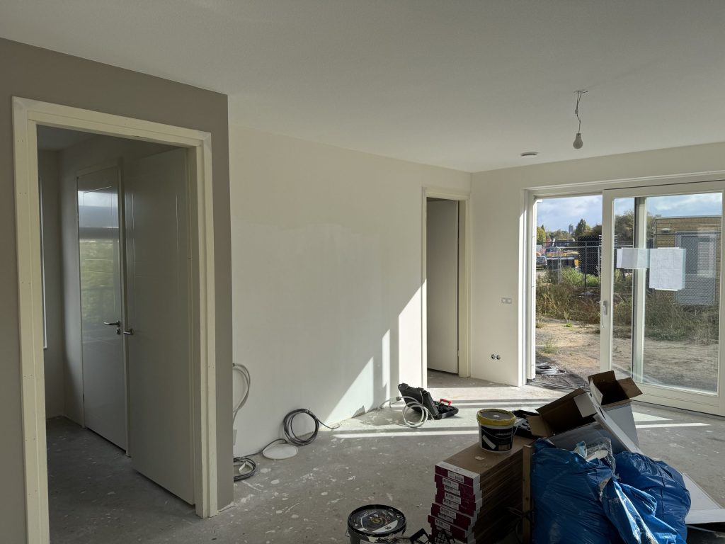 Nieuwe woonkamer tijdens de afwerking met lichte wanden, tuindeuren en verfemmers en dozen op de betonvloer